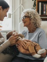 Grandmotherly woman holds baby while smiling at young mother
