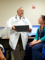 Dr. Ruiz stands and speaks with a group of other providers sitting in a room of computers