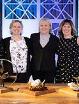 A group of five smiling women standing at a table with awards