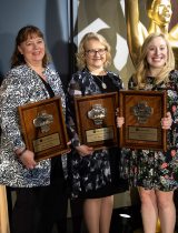 A group of five women hold award plaques