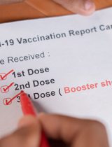 COVID-19 vaccination card in hands showing booster shot box checked