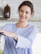 A woman smiles while using a blender