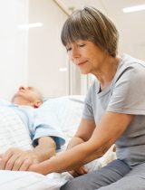A woman holding the hand of a patient in a hospital bed
