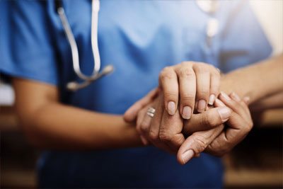 A healthcare provider holds the hand of someone in a comforting manner