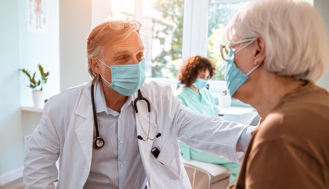 A masked patient and health care provider have a discussion in a clinical setting