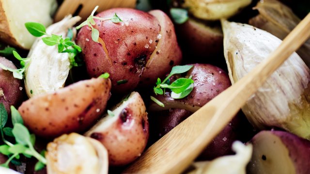 A wooden sppon rests in a red potato salad with herbs and garlic 