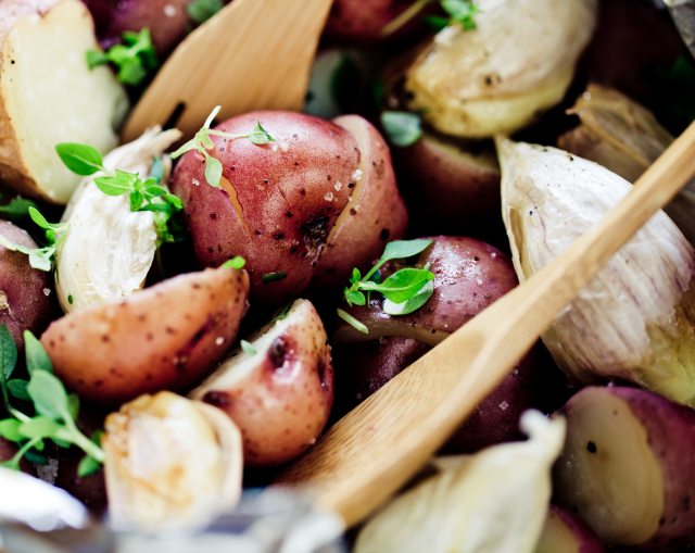 A wooden sppon rests in a red potato salad with herbs and garlic 