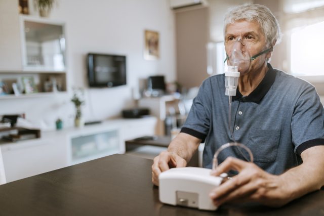 Senior man using an inhaler at home