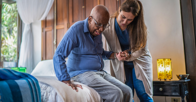 A healthcare provider helps an elderly man stand