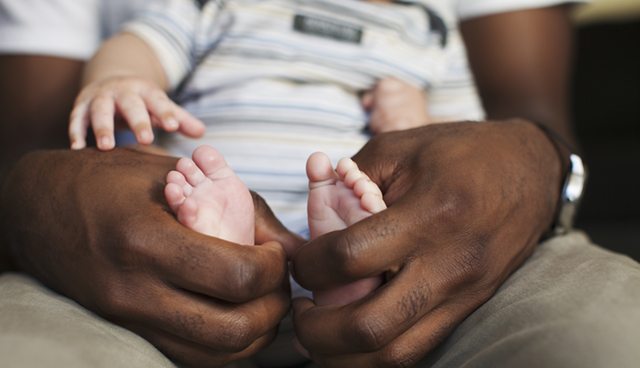 A baby's feet are held by an adult's hands as it they sit on their lap.