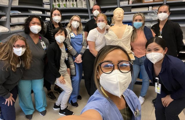 Nurses wearing masks pose for a selfie with a simulation mannequin