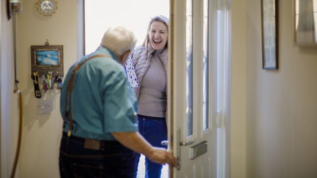 Older man opens door of his home to a happy woman