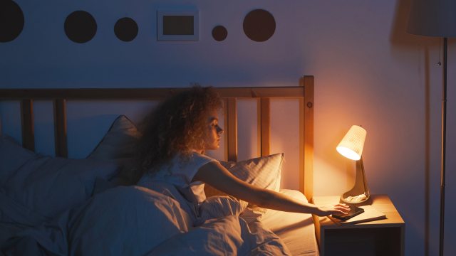 Woman in bed reaches out to cell phone on nightstand