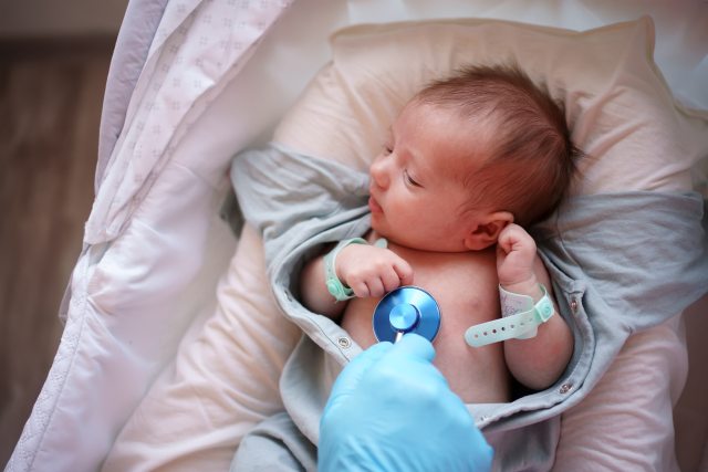 A gloved hand of a doctor holds a stethoscope on the chest of a newborn. 