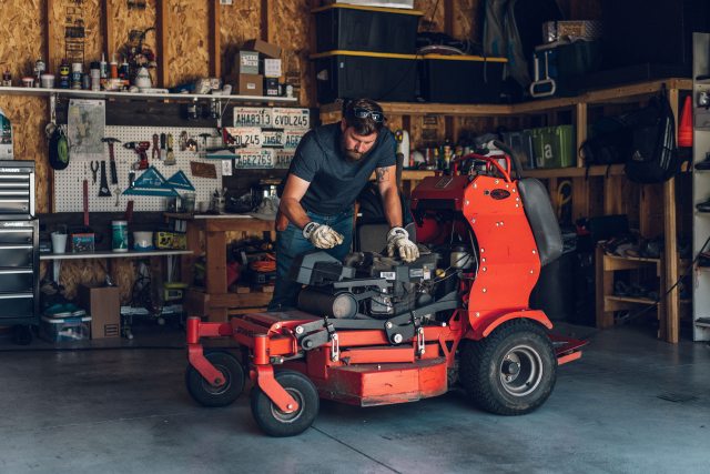 Landscaper Brandon works on the engine of his riding lawnmower in his garage shop