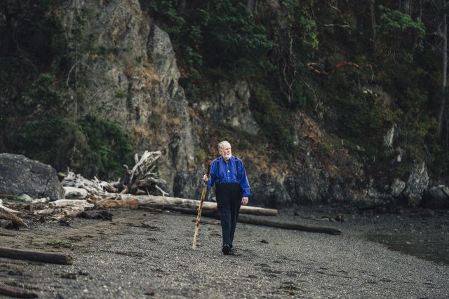 Duncan walks along the beach with a walking stick in Bellingham, Washington