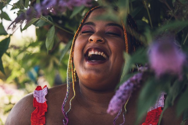 Maisie heartily laughing amongst leaves and blooms in a Wisteria tree