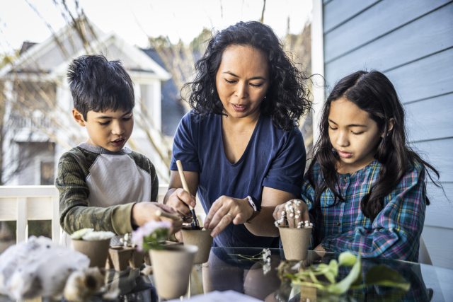 Woman and two young people put plants into pots outside