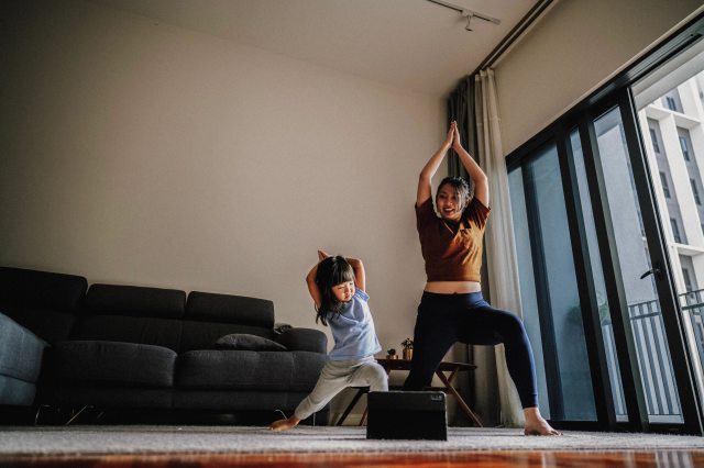 Woman and young girl lunge into yoga pose in living room