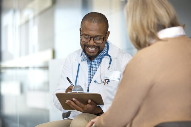 Black doctor writes on a clipboard while talking to a white woman