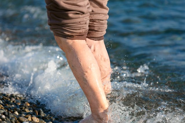 Waves splash on legs of person standing on rocky shore
