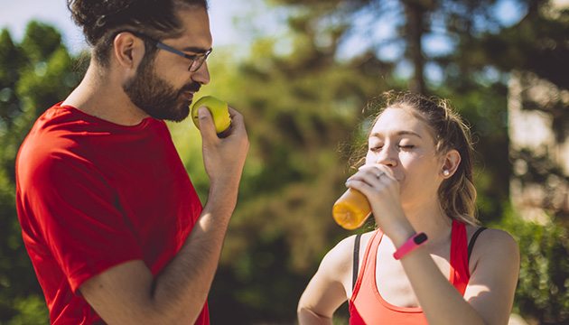A runner eats and apple while another runner drinks juice