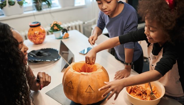 Woman and two children carve a pumpkin on the kitchen table