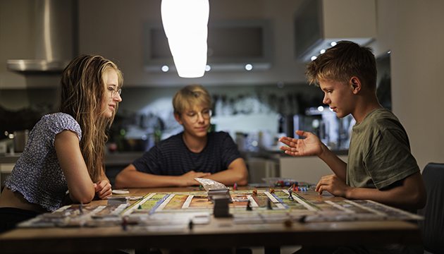 Three young people play a board game at the kitchen table