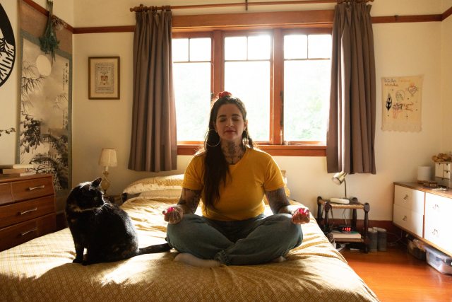 Woman meditating on the floor next to a cat.