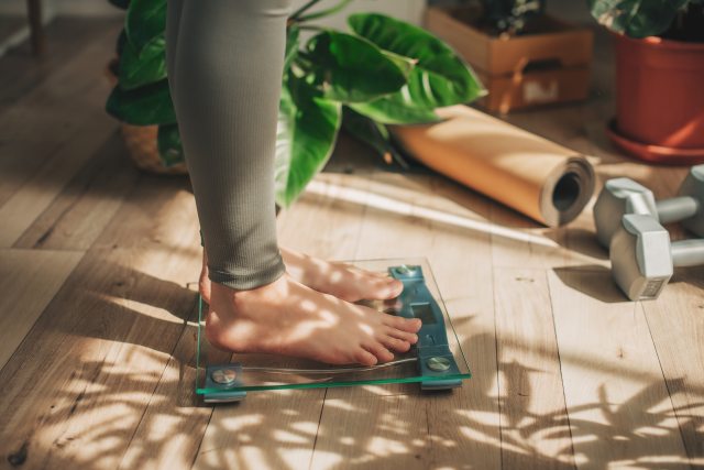 Feet of person standing on a scale next to yoga mat and weight set