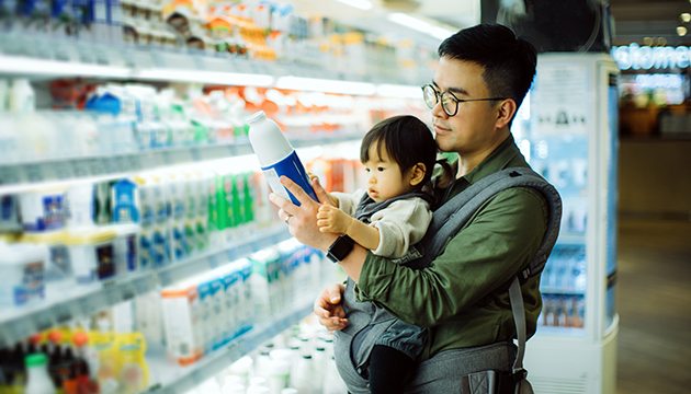 Father holds young daughter as he reads ingredient list on bottle in grocery store