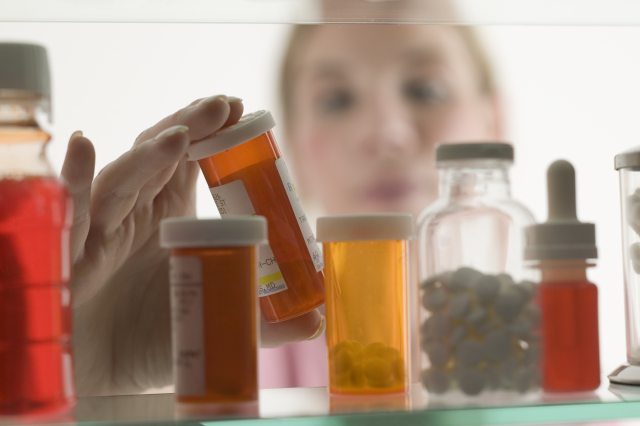 Close-up of bottles of medications in medicine cabinet with blurry image of woman in background