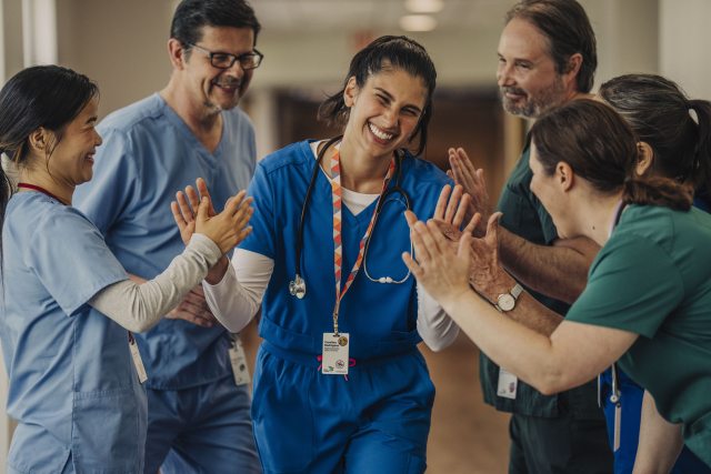 Peacehealth caregiver smiling and walking toward the camera while receiving high fives and pats on the back from coworkers