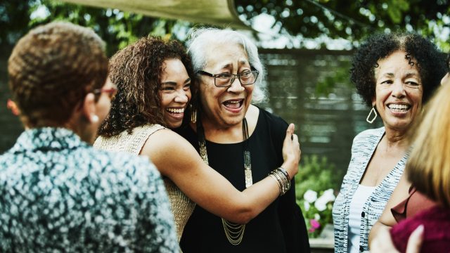 Two women embrace amongst a group of other women smiling and laughing