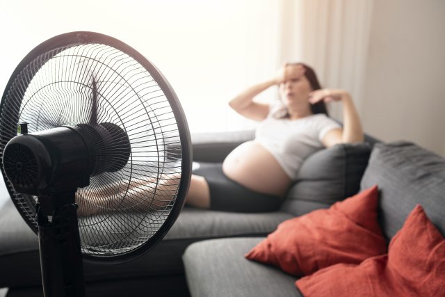 Mom-to-be sits with feet up on couch in front of a fan