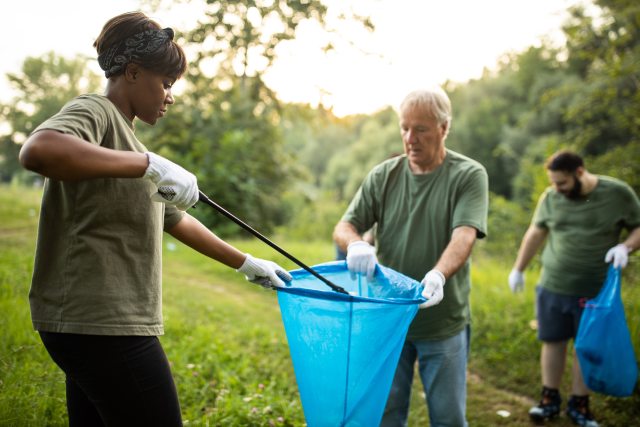 Three people of varied ages clean up trash in a park.