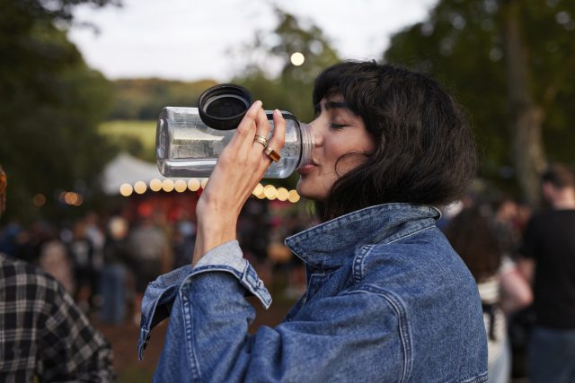 Woman drinking water from a reusable bottle at an outdoor event