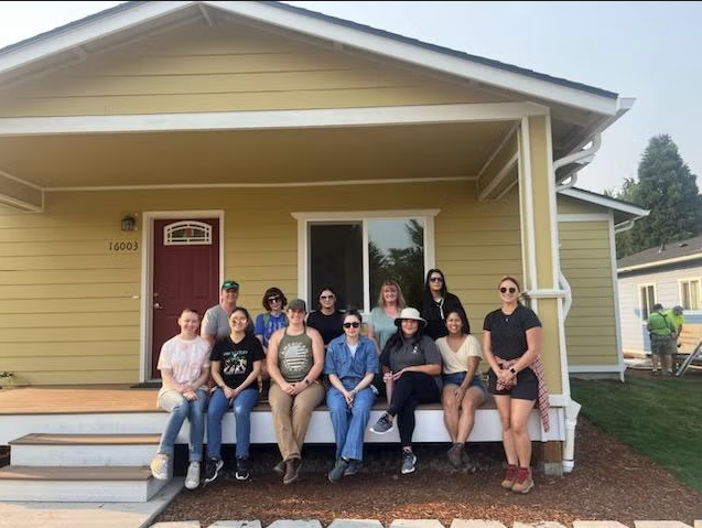 Photo of a group of volunteers sitting on a yellow house porch