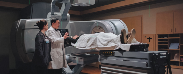 Dr Kim standing next to the linear accelerator with a patient 