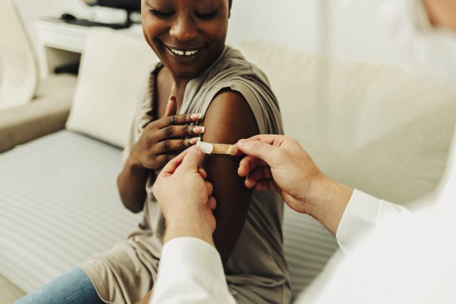 Woman getting a flu vaccine and they're putting the band aid on her arm.