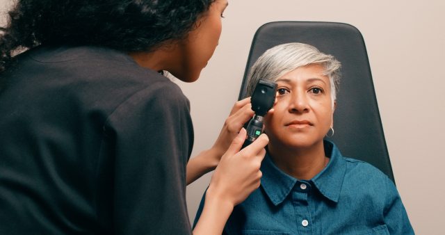 A woman with short gray hair gets her eyes examined by an optometrist.