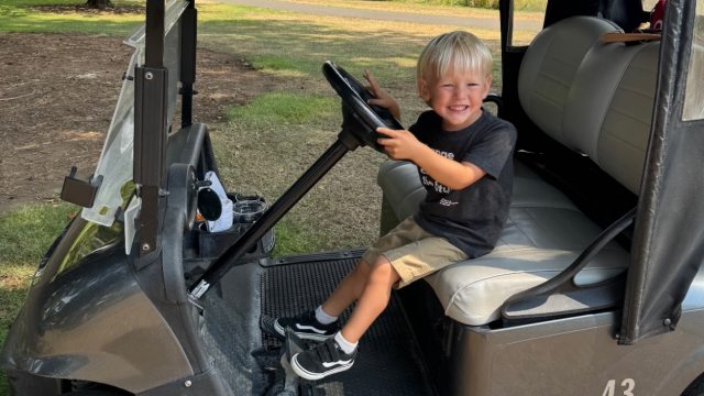 Callan, a young boy, driving a golf cart at the golf tournament
