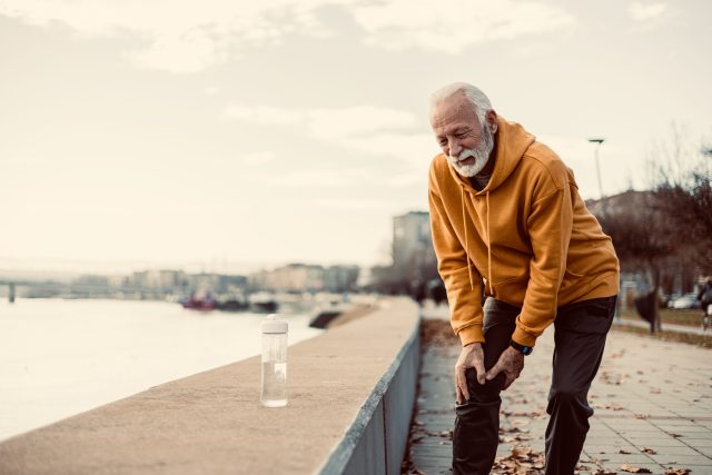 Older man with knee pain walking by river