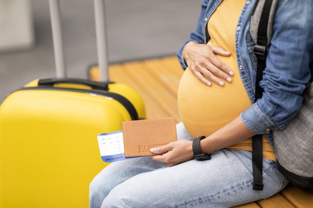 Expectant person holds belly while sitting on bench with luggage 