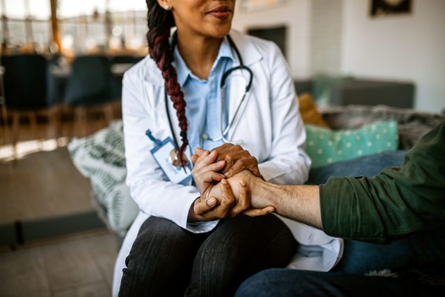 Caregiver holding hands with a patient. Their faces are not seen, only their hands