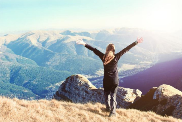 A woman standing on top of a mountain with arms outstretched in a victorious pose