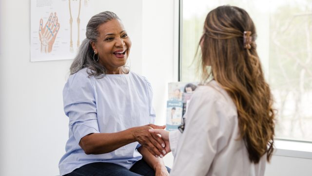 Smiling woman in exam room shakes hand of doctor
