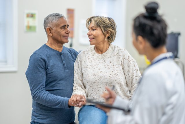 Man and woman smile at each other in exam room with doctor