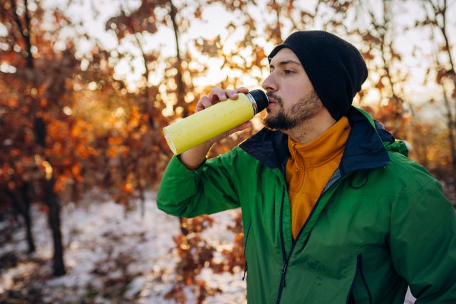 Young man outside in cold weather taking a sip from a thermos.