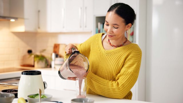 Woman pours smoothie from a blender into a glass